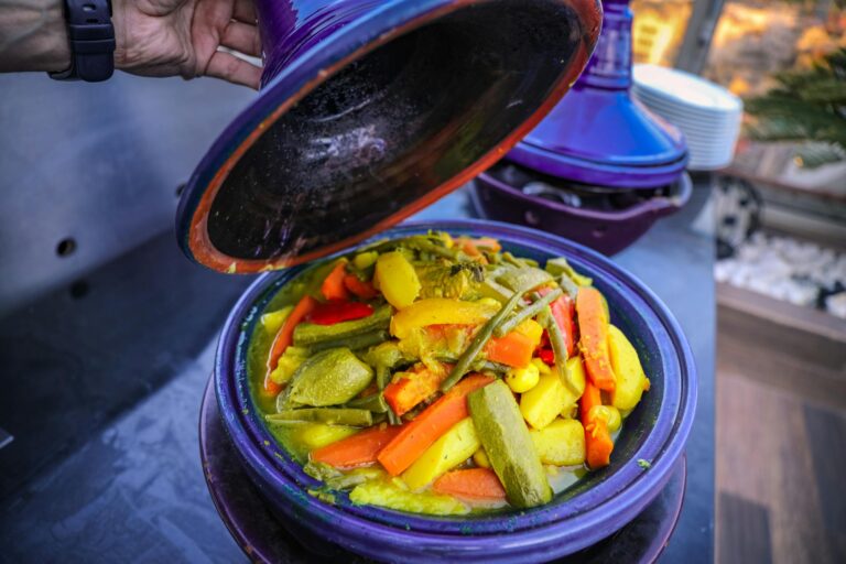 A colorful Moroccan tagine with fresh vegetables being uncovered, showcasing vibrant and healthy cuisine.
