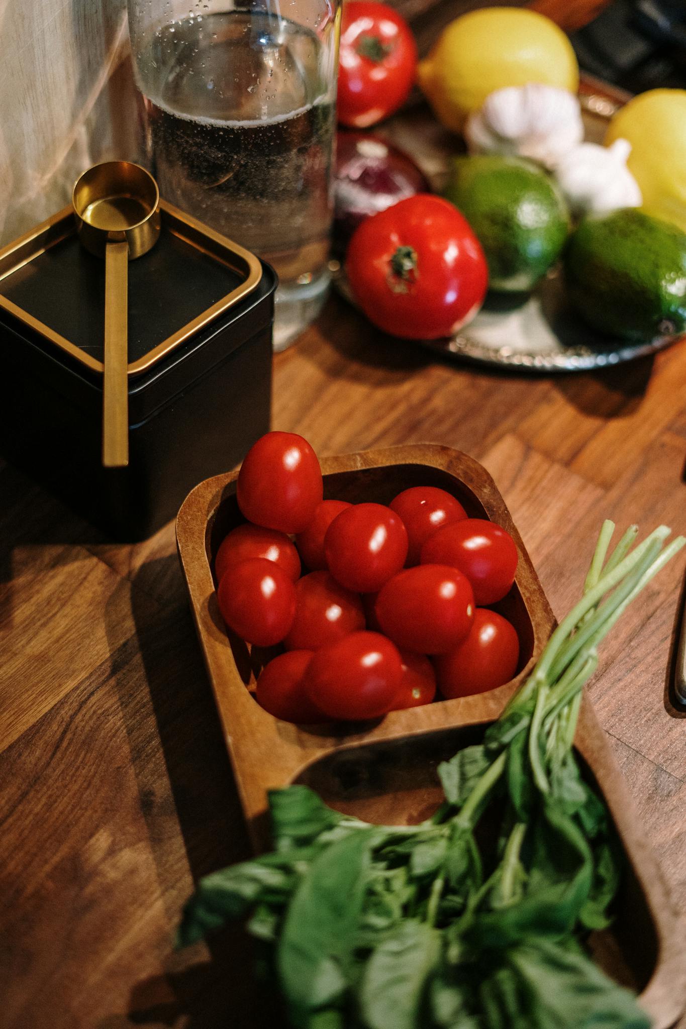 A variety of fresh vegetables including tomatoes, basil, and lemons on a wooden kitchen counter.